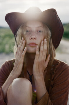 Close-up face of hippie woman in cowboy hat at sunset in meadow.