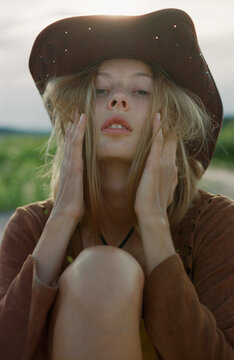Close-up face of hippie woman in cowboy hat at sunset in meadow.