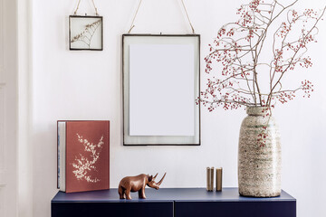 Stylish living room interior with mock up poster frames, navy blue commode, book, decoration and elegant personal accessories in modern home decor.  White wall. Template.