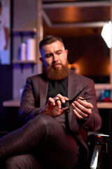 close-up photo of shears in hands of professional male barber, handsome guy in suit examining, checking scissors for future cutting hair of clients, at work place