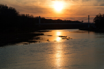 fiery sunset over the calmly flowing Ural river and pedestrian bridge