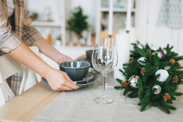 Young woman in plaid shirt sets festive table with fir composition, christmas time