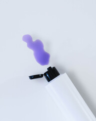 Beauty bottle product shot from top down showing purple liquid spilling out onto a white background. White and black bottle shown from above. Copy space available