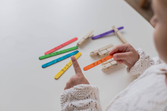 Child solves math examples with wooden sticks , didactic materials , Diy, home education. Mathematics for preschooler.