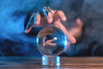Fortune teller is reading the future by a crystal ball on the table in the smoke.