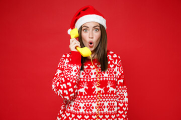 Shocked amazed young Santa woman 20s wearing sweater Christmas hat talking on telephone keeping...