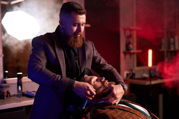 caucasian hipster client man visiting in barber shop shaving beard by professional hairdresser, stylish and and modern beard in salon