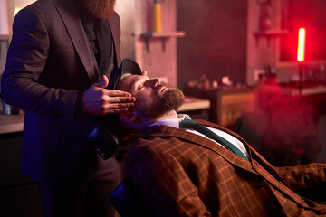confident male barber preparing client for cutting beard, hairdresser is examining his hair...