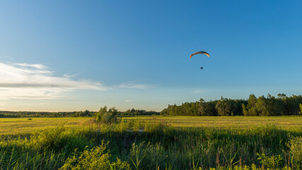 A powered paraglider flying over the idyllic meadow on a sunny day. Summer landscape with moto...