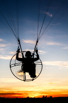 Silhouette of powered paraglider against late day sky. Low flight of paramotor machine during sunrise 