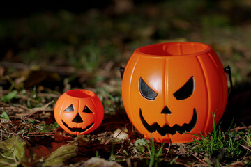 Two Halloween toy plastic orange pumpkins on the ground among leaves, grass and pine needles