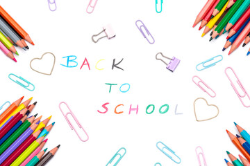 Handwritten back to school sign made of multicoloured pencil crayons. School supplies. Education concept. Colorful pencils, paperclips and paper clamps arranged on white background, top view
