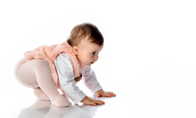 Little cute girl in a warm fur vest sits on the floor of the studio, trying to stand up or crawl to the side