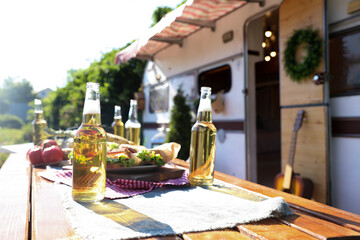 Delicious sandwiches and bottles of beer on wooden table near motorhome on sunny day. Camping season