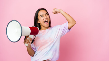 Young asian woman holding a megaphone isolated on pink background raising fist after a victory, winner concept.