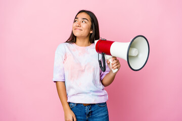 Young asian woman holding a megaphone isolated on pink background dreaming of achieving goals and...