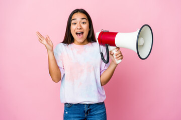 Young asian woman holding a megaphone isolated on pink background receiving a pleasant surprise, excited and raising hands.