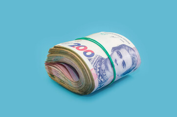 Ukrainian hryvnia tied with an elastic band isolated on a blue background. Money stack. Financial concept. 200 hryvnia banknotes rolled into a roll.