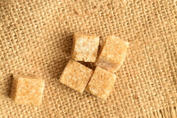 Several cubes of brown sugar, close-up, on a jute fabric.