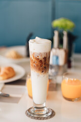 Iced cappuccino coffee in a tall glass cup on table with breakfast background. vintage film color tone.