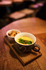 Serving cream soup in a cup with a cup of rusks on a wooden tray