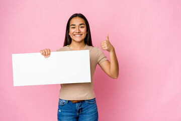 Young asian woman holding a blank paper for white something over isolated background smiling and...