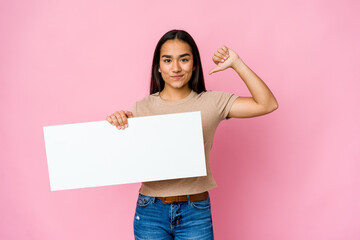 Young asian woman holding a blank paper for white something over isolated background feels proud and self confident, example to follow.