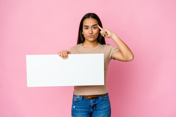Young asian woman holding a blank paper for white something over isolated background pointing temple with finger, thinking, focused on a task.
