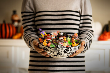 Woman at the front door offering Halloween candies on a nice bowl. Unrecognizable person