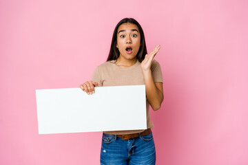 Young asian woman holding a blank paper for white something over isolated background surprised and shocked.