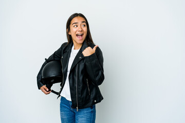 Fototapeta premium Young asian woman holding a motorbike helmet over isolated background points with thumb finger away, laughing and carefree.