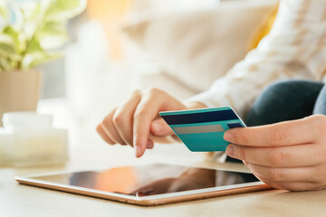 Stock photo of an unrecognizable woman shopping online with her tablet and a credit card from the couch at living room. E-commerce and buying from sofa concept