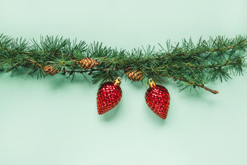 Christmas spruce branch on green background with red toys. Christmas border. Flat lay