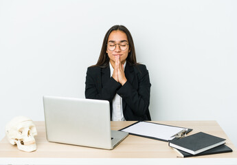 Young traumatologist asian woman isolated on white background holding hands in pray near mouth, feels confident.