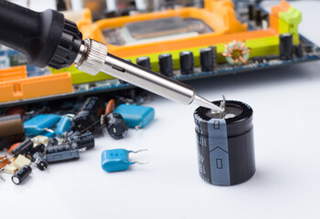 soldering iron on the background of a computer Board and capacitors in soft focus.