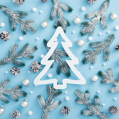 Christmas snowy decoration on pastel blue background. Pine branch and cone, bauble and abstract snowball. Square composition, flat lay. White fir tree shape