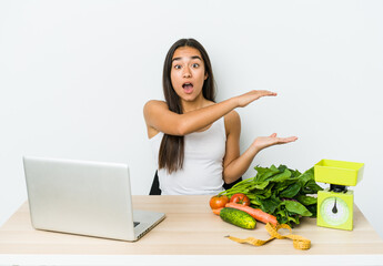 Young dietician asian woman isolated on white background shocked and amazed holding a copy space between hands.