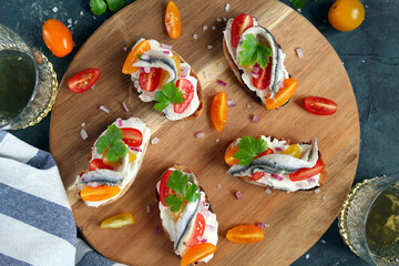 Bruschetta with light cheese, tomato and anchovy served with white wine on dark background. Top view with copy space.