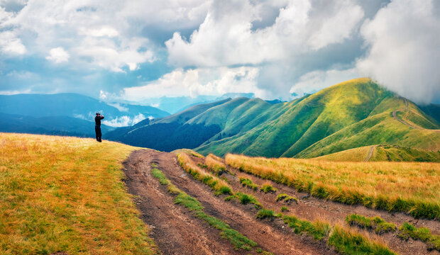 Tourist takes picture of mountain range with old country road. Gloomy summer view Svydovets range, Carpathian mountains, Ukraine, Europe. Traveling concept background.