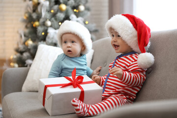 Fototapeta na wymiar Cute children in Santa hats sitting on sofa at home. Christmas celebration