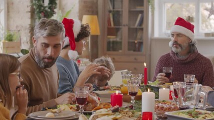 PAN with slowmo of three generations of family sitting at dinner table filled with tasty dishes and chatting while enjoying food on Christmas day
