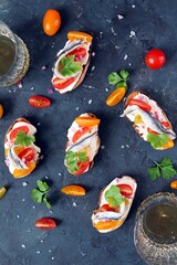 Bruschetta with light cheese, tomato and anchovy served with white wine on dark background. Top view with copy space.
