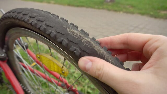 A cyclist inspects a flat torn wheel on a bicycle with his hand, an old tire, industry