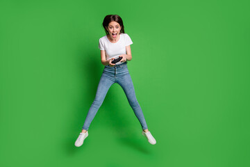 Full size photo of crazy girl jump play video game wear white t-shirt denim jeans isolated on green bright color background