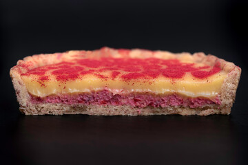 lemon tart with raspberry crunch, lemon curd, raspberry powder decoration, black background, front view