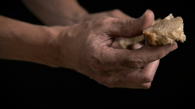 Dirty hands with bread. A view of a hungry man with dirty hand with a piece of bread on the black background.