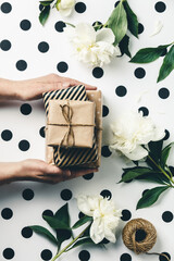 Flat lay arrangement female's hands holding gift boxes among presents and flowers, top view