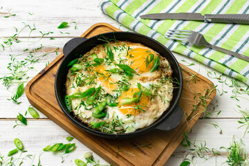 scrambled eggs with greens sprouts and green onions in a pan on a wooden background.