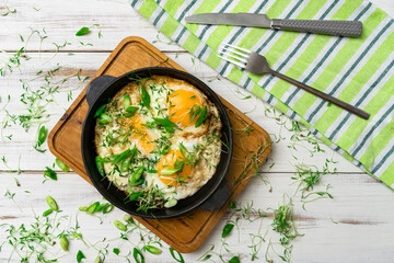 scrambled eggs with greens sprouts and green onions in a pan on a wooden background.