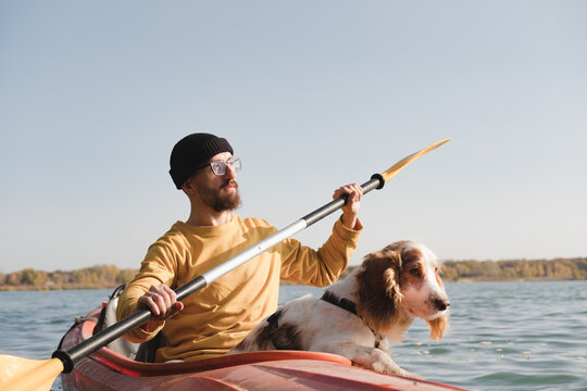 Kayaking with dogs: man rowing a boat on the lake with his spaniel. Active rest and adventures with pets, riding a canoe with dog